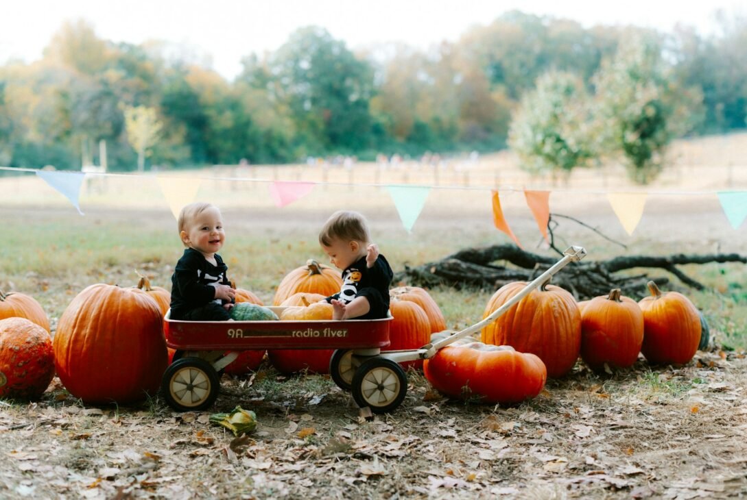 Two babies in a wagon surrounded by pumpkins.