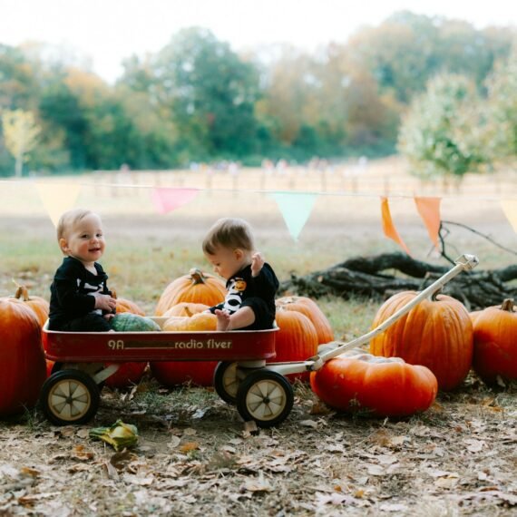 Two babies in a wagon surrounded by pumpkins.