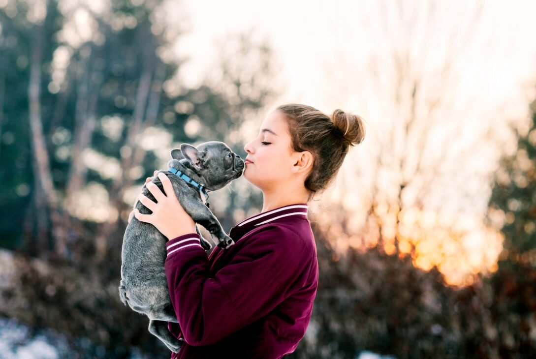 Girl kissing french bulldog puppy outdoors