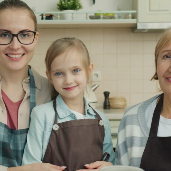 Three smiling women in a kitchen wearing aprons.